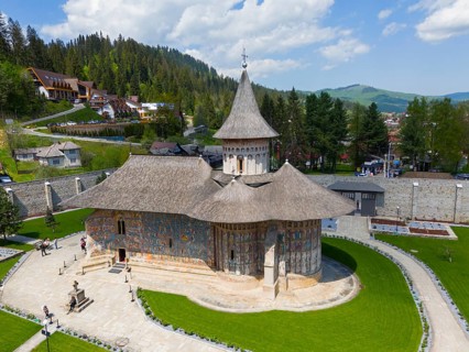 Orthodox church with frescoes surrounded by green countryside and wooded hills under clear blue