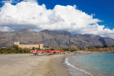 Red umbrellas on the beach in Frangokastello on the Libyan Sea, in the back the Venetian fortress