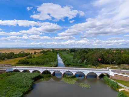 View over a bridge over a river with green surroundings and a sky full of clouds, aerial view,