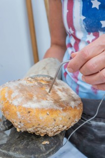Woman measures the temperature of a loaf of bread with a measuring device device in her hand,