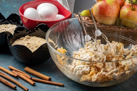 Grated apples and quark are mixed in a bowl, surrounded by other baking ingredients
