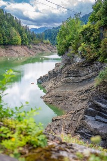 Clear lake with rocky coast, surrounded by green trees and calm water surface, Krumbach,