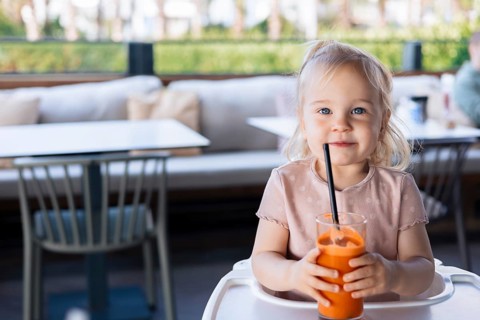 Girl toddler drinking fresh orange carrot juice in outdoor cafe