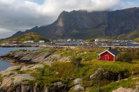 Lonely red Rorbuer hut on a green meadow with a view of pure and dried fish racks in front of