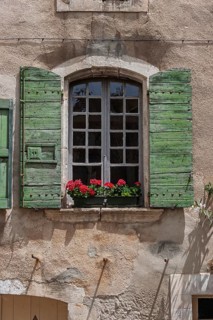 Window with green shutters and red geraniums on an old stone wall, Provence, France