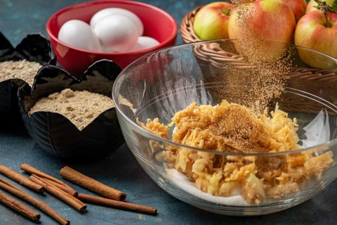 Grated apples sprinkled with cinnamon in a bowl, surrounded by other ingredients
