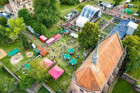Aerial view of a festival with people, tents and a stage in green surroundings, Calwer
