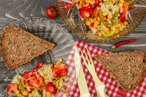 Salad plate with slice of brown bread and fresh vegetables on a rustic wooden table with checkered
