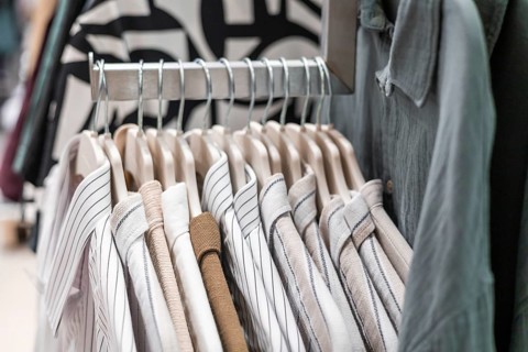 A rack displaying neatly arranged striped and solid shirts in a retail store. The shirts are