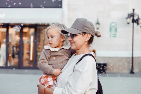 A woman holds her young daughter close as they watch bubbles float in the air. The city square is