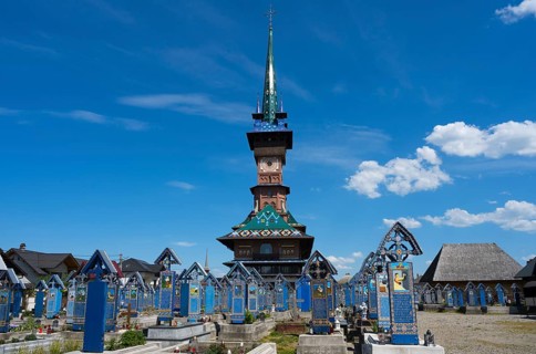 View of a church with colorful tombs under a cloudy sky, traditional wooden graves, Merry Cemetery,