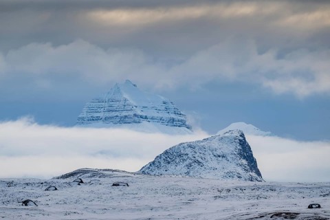 Large rock behind clouds cover one of the three mountains Tee Kroner, Kongsfjord or Kongsfjorden,