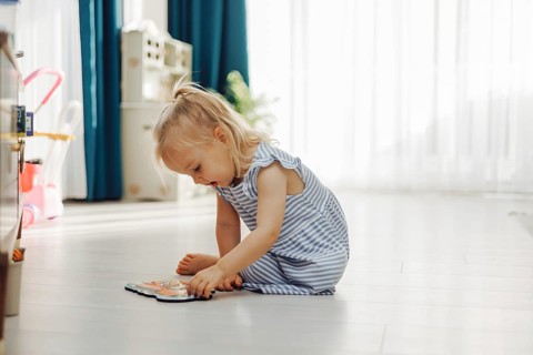 Young girl focused on a colorful toy while sitting quietly on the floor indoors. Wooden