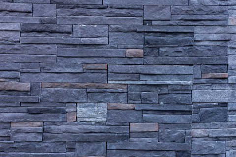 A textured wall made of dark stone bricks arranged in a pattern. The stones vary in size and color,