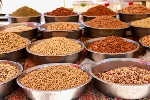Assorted nuts and grains displayed in metal bowls at a marketplace