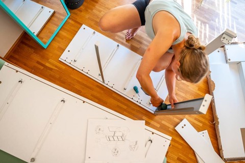 Young woman setting up a shelf, furniture assembly with screwdriver, IKEA furniture in a new