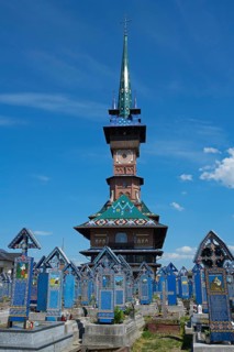Historic church tower overlooks ornate tombs under a clear sky, traditional wooden grave sites,