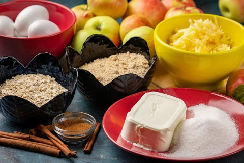 Baking ingredients such as grated apples, sugar, oats, quark, nuts, eggs and cinnamon on a dark