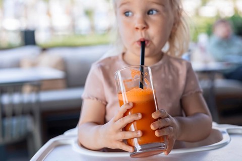 Girl toddler drinking carrot juice in cafe
