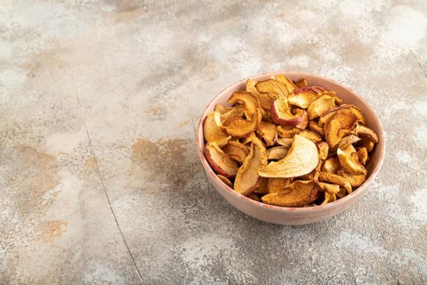 Dried Apples in ceramic bowl on brown concrete background. Side view, copy space, flat lay. healthy