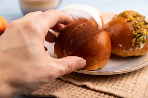 Maritozzo traditional Italian bun dessert with hand, cup of coffee, on blue wooden background with