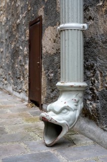 Detailed view of an antique rainpipe outlet in the shape of a decorative gargoyle figure. The