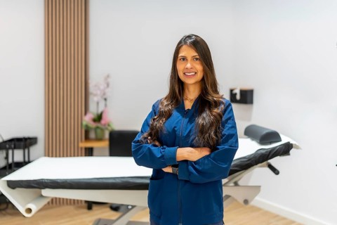 Smiling female professional standing confidently with arms crossed in a modern aesthetic clinic or