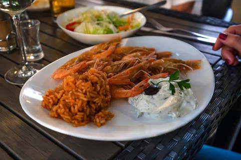 Grilled prawns served with red rice and creamy tzatziki with an olive, served in a Greek garden
