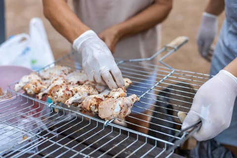 Hands placing marinated chicken pieces on a grill. The scene shows a close-up of food preparation