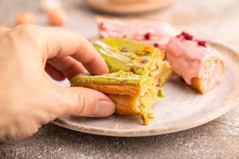 Glazed Eclairs on brown concrete background and green linen textile with hand, cup of coffee, side