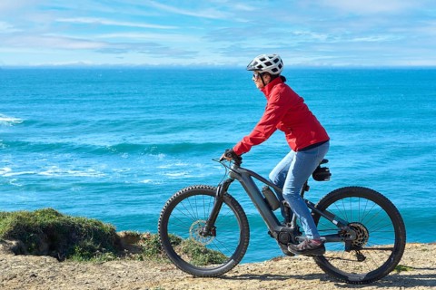 Active senior woman riding her electric mountain bike on the rocky cliffs of Peniche at the western