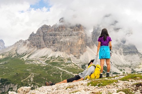 Woman helping exhausted hiking partner boyfriend dragging in Dolomites mountains. Teamwork