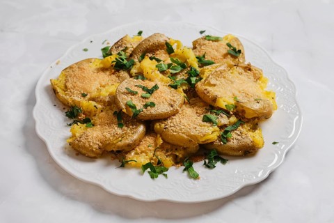 Crispy smashed potatoes are placed on a white plate and topped with fresh herbs. This dish is in a