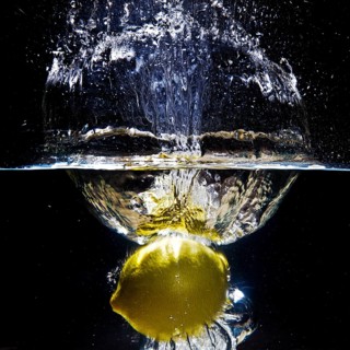 A fresh yellow lemon (Citrus limonum) falls into the water, creating a splash and air bubbles,