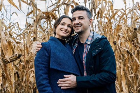 A happy couple in love stands in autumn near a cornfield. A man in a shirt and jacket hugs a woman