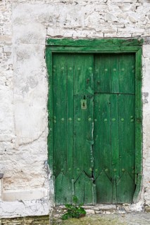 An old green wooden door in a weathered stone wall, looks rustic and historic, Cyprus