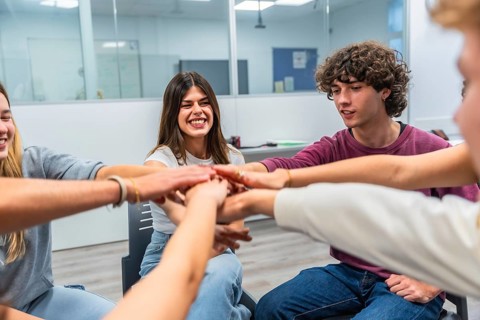 Group of young students gathered in a circle in a classroom, stacking their hands together,
