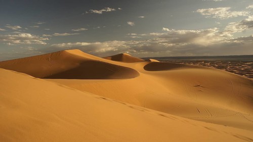 Majestic sand dunes under a golden, cloudy sky in the desert, Merzouga, Erg Chebbi, Morocco