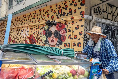Bangkok, Thailand. August 24th 2026. A man pushes a cart selling fresh fruit past colourful street