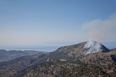 Smoke rises from a forest fire in a mountainous landscape, the sky is clear and blue, Majorca,