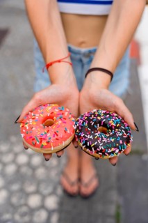 Woman's hands presenting two delicious frosted donuts with colorful sprinkles, offering a sweet