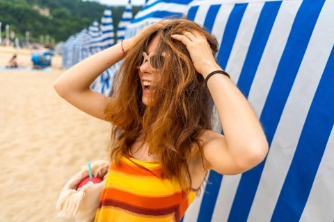 Young reddish haired woman laughing heartily. Playfully running hands through her hair. Wearing