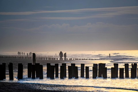 Winter on the North Sea, sunset at sea, beach walkers, coastal protection, through wooden posts,