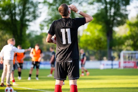 Soccer player wearing number eleven drinking near the sideline during a football match on a sunny