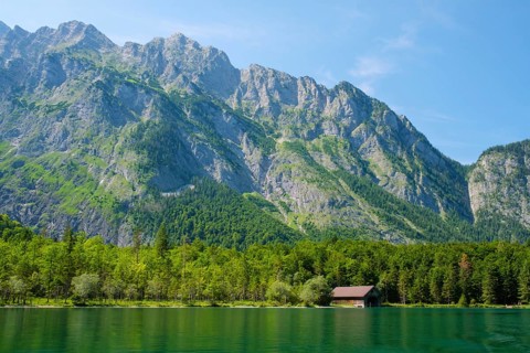 Lakefront view of Konigsee in Bavaria, Germany, with a small boathouse below the Berchtesgaden Alps