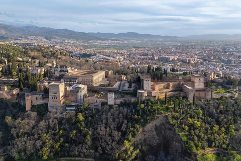 Wide aerial view of the Alhambra palace and fortress complex above Granada, Spain, surrounded by