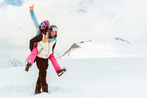 Caucasian happy adult skier couple together piggyback arms up walk together enjoy snowy day freedom
