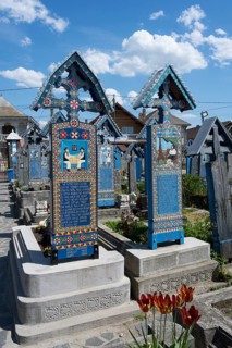 Two richly decorated tombs under a blue sky in a peaceful cemetery, traditional wooden grave sites,