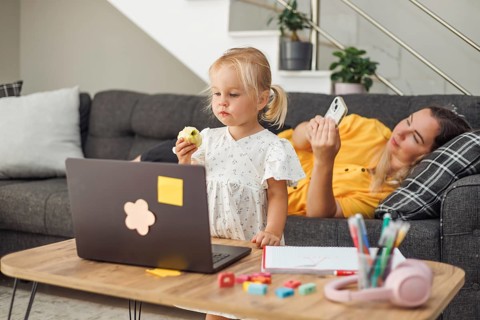 Young blond European girl eating sandwich with laptop on table. Pregnant blond European woman
