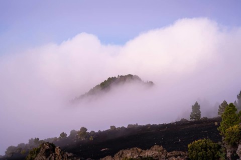 View from Mirador Astronómico del Llano del Jable of evening clouds moving across a hill at sunset.
